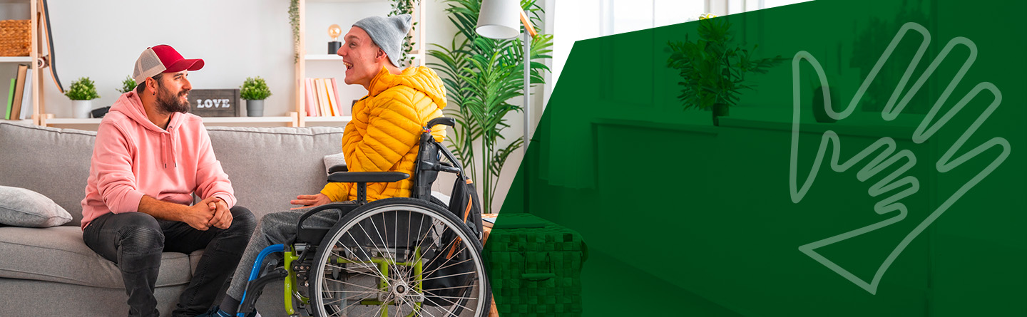 Heilerziehungspflege Header: Eine Betreuungsperson sitzt auf einem Sofa und unterhält sich mit einer Person im Rollstuhl